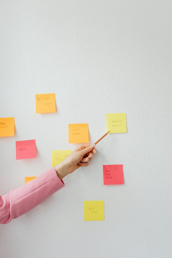 pexels-photo-7680054-7680054 A person in a pink sleeve pointing at colorful sticky notes on a wall during a planning session.
